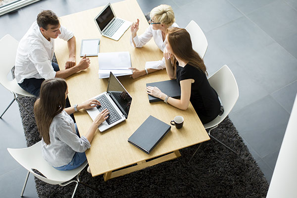 Overhead view of male and three females working at conference table with laptops and notebooks